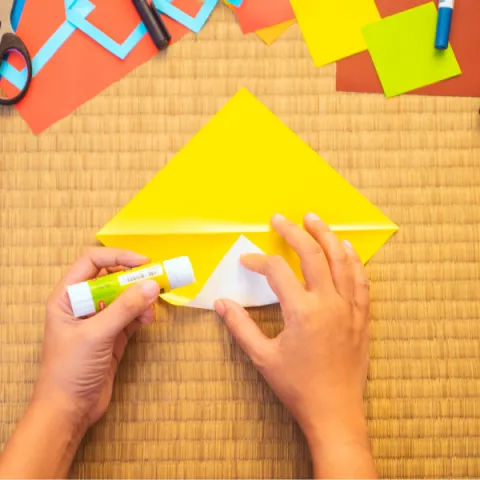 a pair of hands folding a yellow piece of origami paper