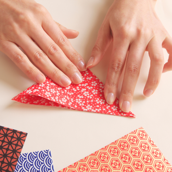 Two hands folding a patterned piece of paper.