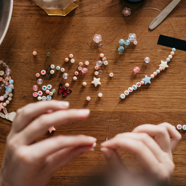 Two hands creating a bracelet with thread and beads.